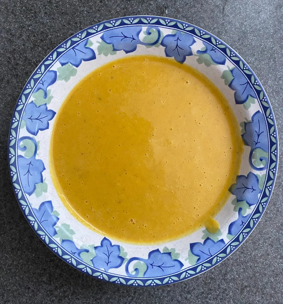 A bowl of curried butternut squash soup, smooth and golden orange, on a blue and white patterned plate.