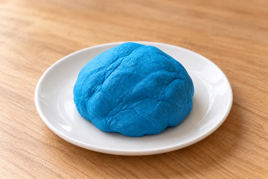A smooth ball of bright blue homemade play dough on a white plate.